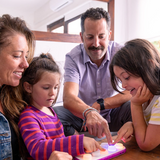 Family of four, including two adults and two children, interacting with a tablet device.