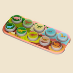 A children's dinosaur game featuring ten round dino-shaped pieces with different dinosaur illustrations, arranged on a colorful printed tray with a pink border.