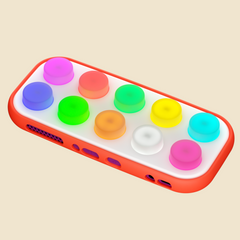 A rectangular electronic device with a bright red bumper and a white face, featuring ten circular buttons in various colors including purple, blue, green, orange, yellow, cyan, and pink. The device is shown floating against a solid light beige background.