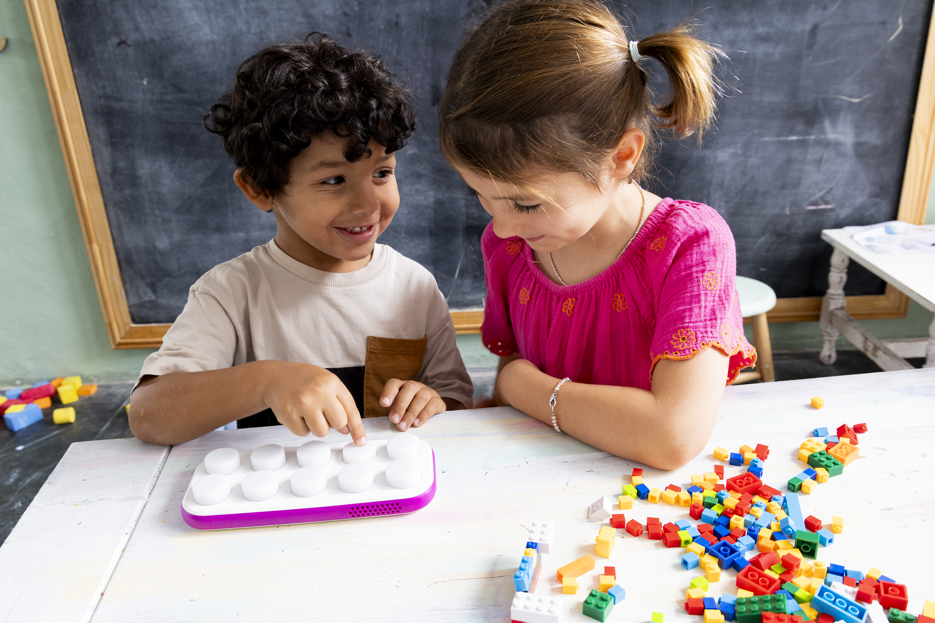 Two children playing with a Boppo, besides colorful building blocks at a table