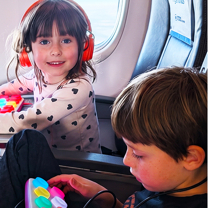 Two children on an airplane with a portable travel tablet and colorful toy.