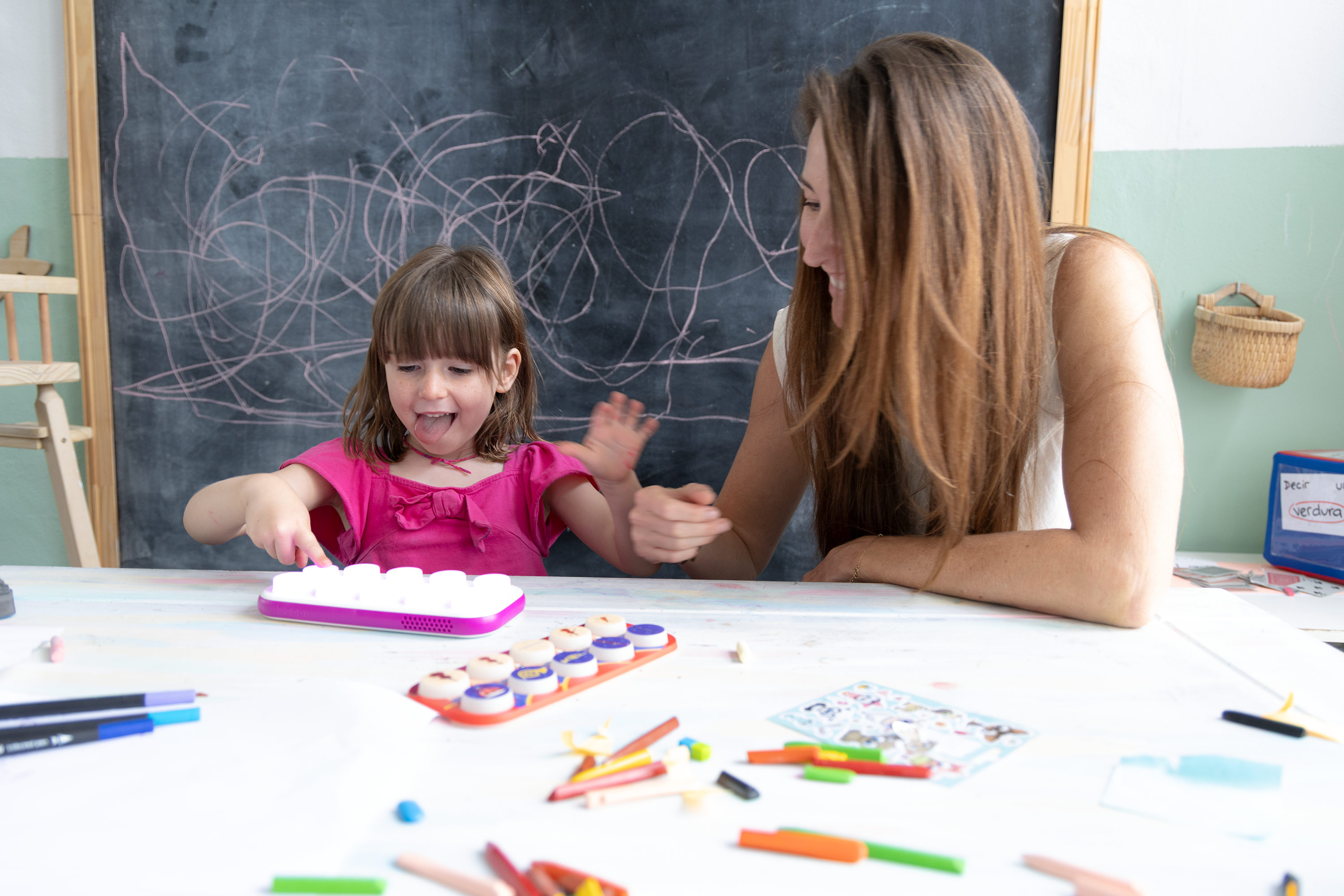 Woman and child engaged in an art activity with crayons and a blackboard in the background