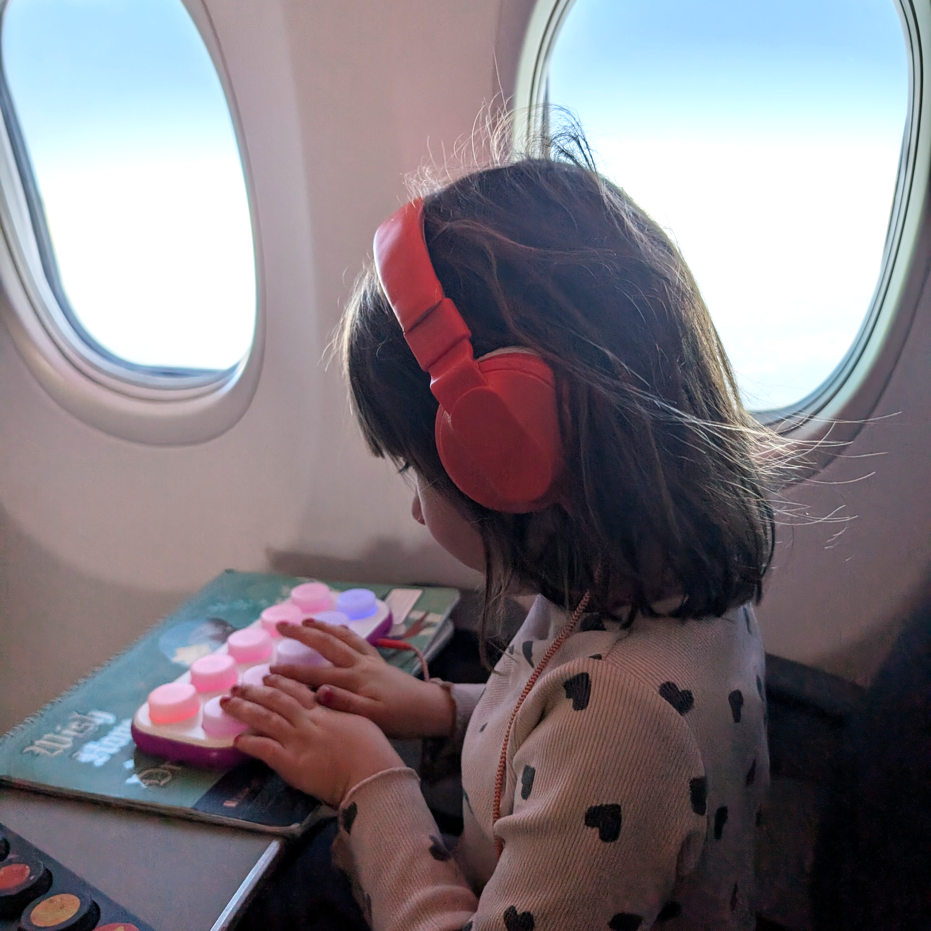 Child wearing red headphones sitting by an airplane window with a Boppo