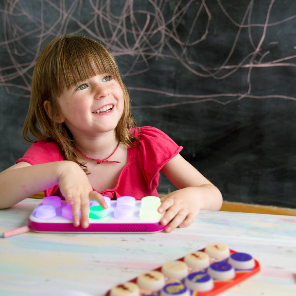 Young girl playing with a colorful toy on a table against a chalkboard background