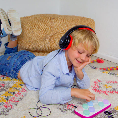 Child wearing headphones lying on a colorful rug with a Boppo