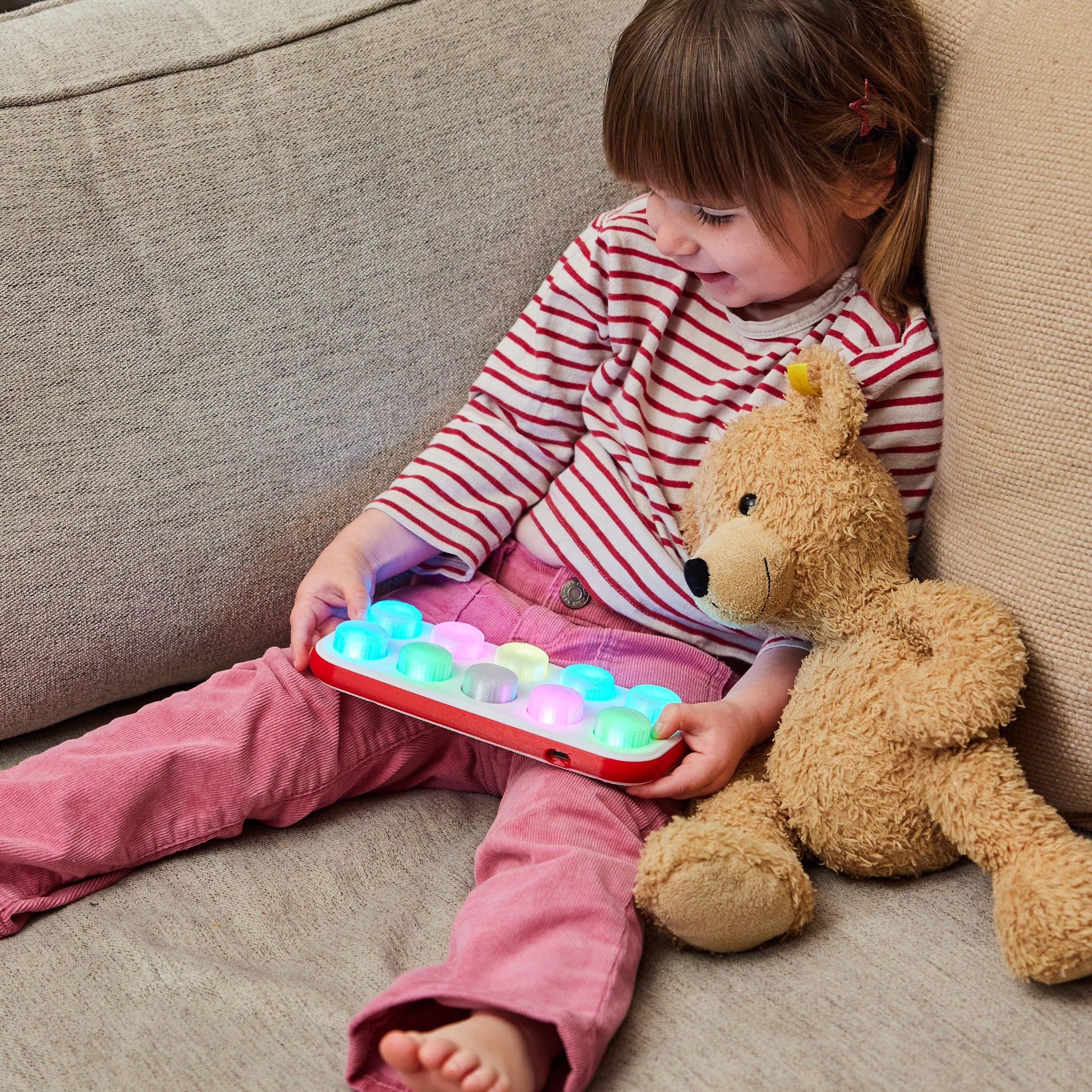 Child sitting on a couch with a Boppo tablet and teddy bear