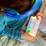 Person wearing blue headphones and holding a colorful device with lights, sitting on a couch.
