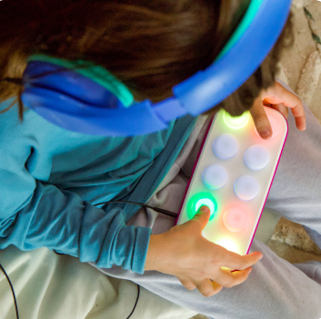 Person wearing blue headphones and holding a colorful device with lights, sitting on a couch.